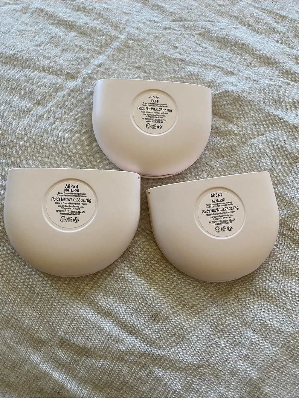Rare Beauty pressed powder compacts in warm beige and tan tones